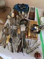 Overview of various silverplate flatware and serving pieces arranged on table including spoons, wooden handled knives, nutcrackers, and storage items.