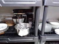 Sunbeam stand mixer with extra bowls and several plates around on the shelves.