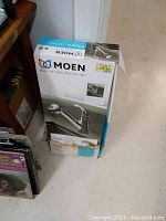 Box of Moen Integra CA87315C kitchen faucet showing front and side images. Clearly visible Moen branding and model information. Price tag attached to box showing $139.99. Box has water damage at bottom corner.