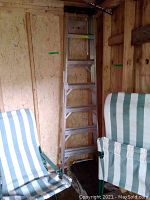 Full view of Featherlite aluminum ladder showing its height and rung style with wear marks, positioned in a shed corner beside striped folding chairs.