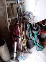 Golf clubs, ski poles, bike pump and golf bags stored in garage corner on concrete floor