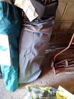 Three camping chairs in storage bags showing labels and carrying cases, stored in a basement setting