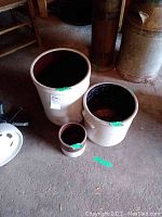 Three crocks of various sizes arranged on a concrete floor showing wear and age.