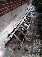 Two aluminum extension ladders stacked against exterior brick and stucco wall, showing side rails and rungs