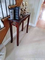 Wooden console table against wall with decorative carved apron and slender legs, worn finish visible.