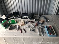 Wide view showing various medical instruments and supplies laid out on a white sheet, including syringes, glasses, diagnostic kits, and cases.
