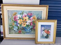 Two framed floral paintings displayed together, one is larger impressionistic bouquet with gold and cream frame, the other smaller floral still life in gold and white frame.