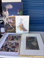 Four framed art prints displayed on a table with Shakespearean theme and costumed crowd visible.