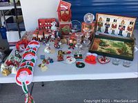 Table display of assorted Christmas decorations including crocheted Santas, bells, glass candlesticks, nutcracker figurines, snowmen, and ornaments.