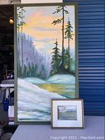 Full view of two framed paintings against a blue door and outdoor setting
