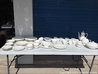Overall view of white porcelain dinnerware set on table including plates, platters, cups, saucers, pots, tureen, gravy boat