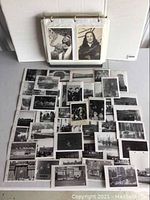 Two-ring binder propped open with two photos visible and a pile of loose black and white photographs below