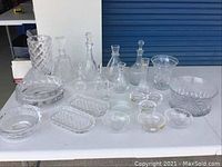 Full view of all crystal and glassware items including decanters, bowls, trays, and small dishes shown on white table.