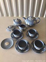 Front view of all pieces: teapot, sugar bowl with lid, creamer, 3 cups and saucers, underplate