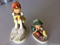 Two Goebel Hummel porcelain figurines, girl with geese and boy with bird on table