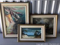 Group view of three framed paintings leaning against wall