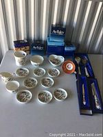 Full view of various Aynsley china items including plates, mug, bowls, and boxed utensils on a table.
