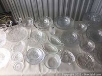 Full overview of the assorted glassware and crystal pieces laid out on a white cloth, showing variety of shapes and patterns