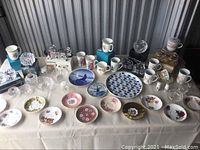 Wide view of teacups, saucers, and crystal decorative items on a table, showing variety of designs and conditions