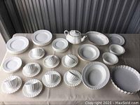 Photo showing full collection of white porcelain dinnerware including plates, teapot, bowls, cups and saucers all with fluted/ribbed design.
