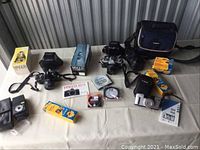 Overview of all cameras, lenses, flash, film boxes, filter, compact camera and bag on table