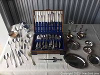 Overview of all flatware pieces laid out on a white surface including the wooden box and the various small tableware pieces.
