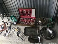 Full view of all flatware and serving pieces arranged on table, including knives, forks, spoons, trays, and other utensils with visible use wear.