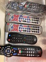 Photo showing 5 remotes including two silver Shaw branded remotes with red and blue buttons, a Rogers branded black remote with colorful buttons, a black remote and one wrapped remote