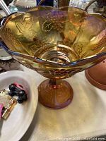 Side view of an amber iridescent carnival glass bowl showing the scalloped edge and pedestal base.