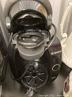 Front view of the Bosch K-Cup coffee brewer showing the dispensing area with circular power button and logo on the black body.