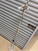 Full side view of the white cast iron floor lamp standing upright showing the double bulb sockets and pull chains, with the brown cord hanging down.