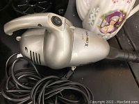 Silver handheld EuroPro vacuum with cord coiled beside it, showing power button and side vents.