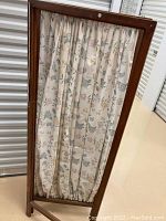 Front view of a wooden framed fabric room divider with floral patterned fabric panel.