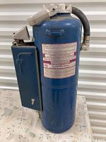 Full view of the blue dry chemical fire extinguisher with attached black hose and metal mounting bracket with key lock.