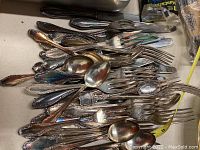 Mixed flatware pieces including forks, spoons, and knives with various designs and tarnishing.