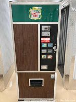 Front view of vintage Canada Dry soda vending machine showing soda selection buttons and coin slot, wood panel front, and green Canada Dry logo.