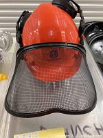 Front view of the orange Husqvarna helmet with black mesh face shield and ear protection cups.