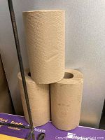 Photo showing three rolls of kraft paper towels stacked, two at the bottom and one on top.