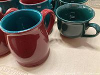 Photo showing multiple ceramic mugs with red exterior and teal interior alongside mugs in teal exterior and red interior colors.