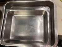Top view of two nested rectangular stainless steel serving pans showing size difference and surface wear.
