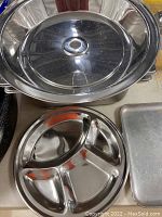Photo showing large round stainless steel covered serving platter with glass lid and round silver metal divided serving platter with three compartments