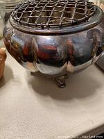 Side view of the 1881 Rogers silver warmer showing scalloped body and tripod feet with metal grid on top.