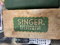 Box top showing 'SINGER BUTTONHOLE ATTACHMENT' label in green with beige background and some wear marks.