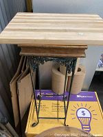 Front angled view of the small wooden cutting board mounted on the two-legged metal stand with detailed scrollwork.