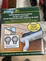 Two Schmidt water drain filter guards in original packaging showing product features, installation, and caution about reducing blockages.