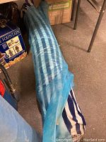 Blue striped fabric roll on floor, wrapped and partially covered with plastic.