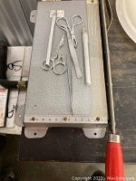 Image showing vintage metal tweezers, small scissors, a long pair of tweezers, exacto knife with red handle placed on a metal paper cutter base with ruler markings.