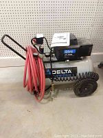 Full view of Delta Shop Master oil-free air compressor with red hose coiled on front, two large black wheels, and handle.