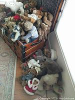 Wide view of collection of stuffed bears piled in wooden chest and spilling on floor including white bunny and bears with clothing.