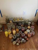 Multiple glass jar candles of various sizes arranged on floor with a metal warming plate